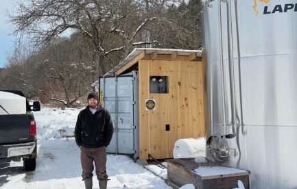 Brendan standing in front of his pumphouse and sap tank
