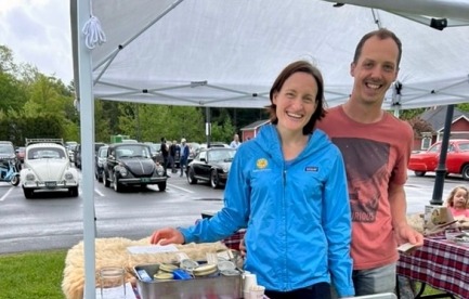 Matt and Ari of Make Do Farm stand smiling behind their white board sign at the first 2025 Randolph Farmer's Market