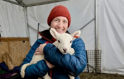 Ari of Make Do Farm grins while holding an adorable lamb