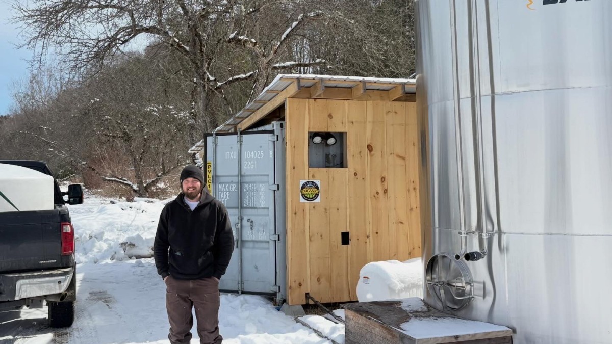Brendan standing in front of his pumphouse and sap tank