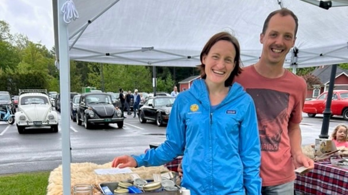 Matt and Ari of Make Do Farm stand smiling behind their white board sign at the first 2025 Randolph Farmer's Market
