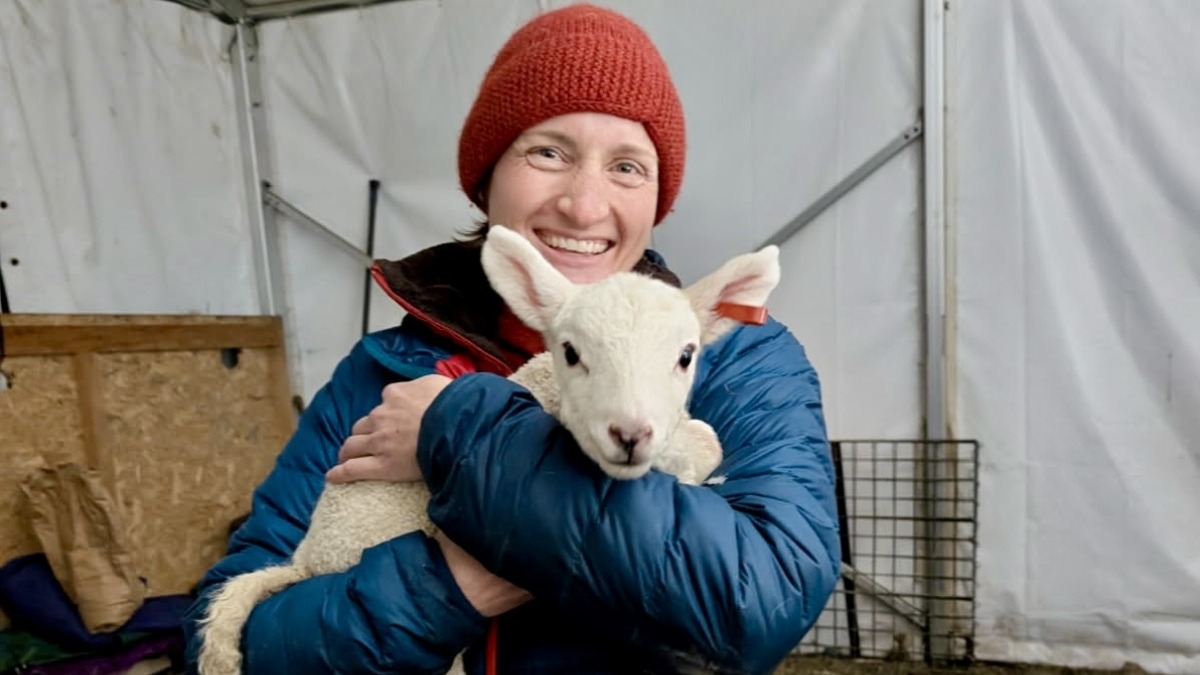 Ari of Make Do Farm grins while holding an adorable lamb