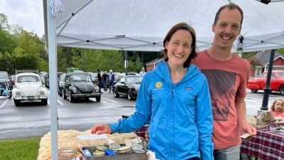 Matt and Ari of Make Do Farm stand smiling behind their white board sign at the first 2025 Randolph Farmer's Market