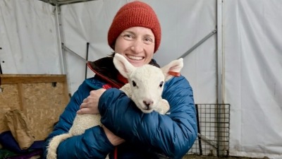Ari of Make Do Farm grins while holding an adorable lamb